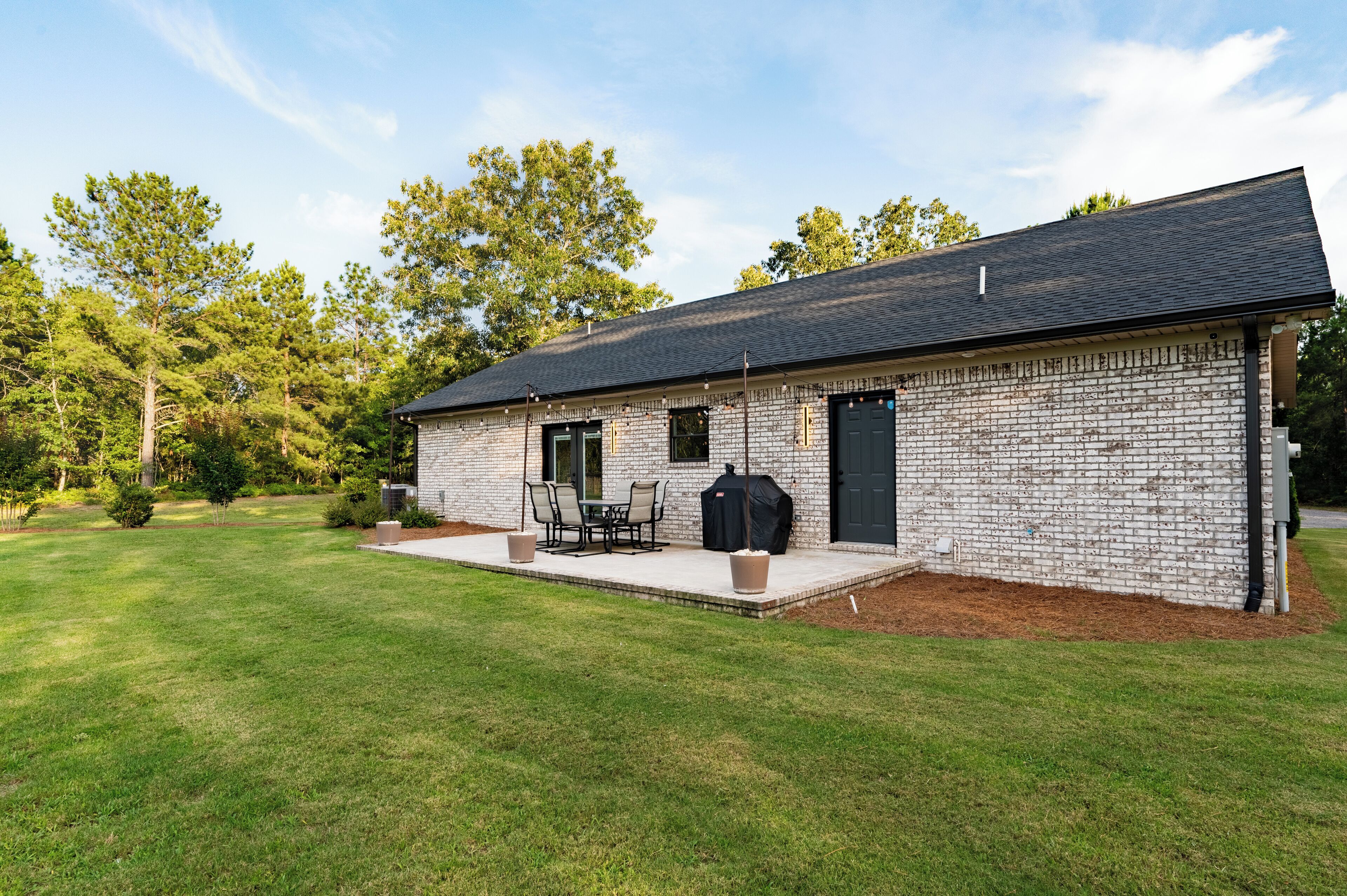 A single-story brick house with a covered patio, a grill, and a door.