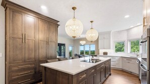 Une cuisine spacieuse avec des meubles de couleur bois foncé, un grand îlot central et des luminaires suspendus.