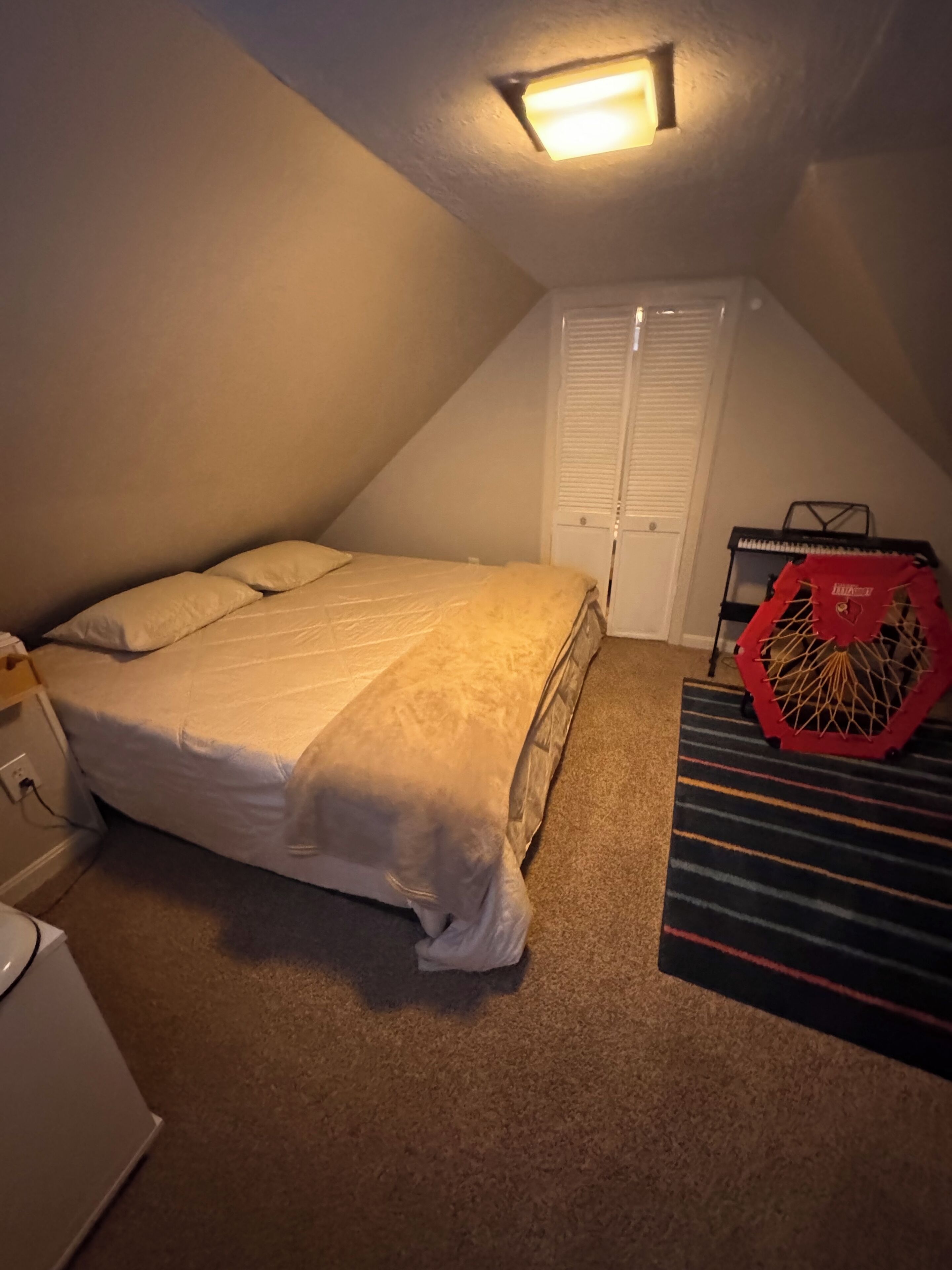 Ein kleines Schlafzimmer im Dachgeschoss, schwach beleuchtet, mit einem Einzelbett, einem kleinen Schreibtisch und einem roten Trainingsrad.