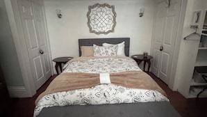 A bedroom with a large bed, two bedside tables, a decorative wall piece, and a wardrobe. - Cozy Derby Home
2 Bedroom Shotgun style home, with Large Adorable Loft (Louisville)