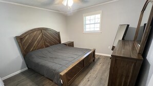 A bedroom with a wooden bed, a nightstand, a dresser, and a window.