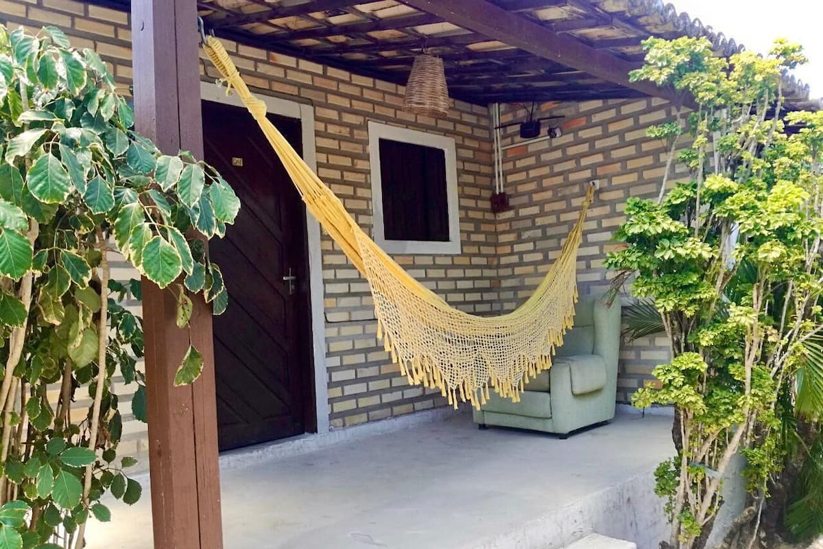 Un hamac sous une pergola en bois, un canapé vert et un mur de briques avec une fenêtre.