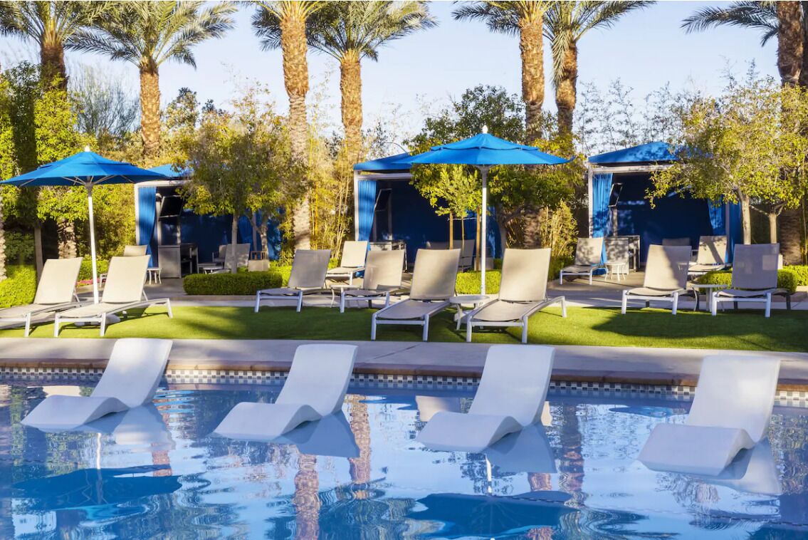 Un espace piscine agrémenté de chaises longues et de parasols, entouré de palmiers.