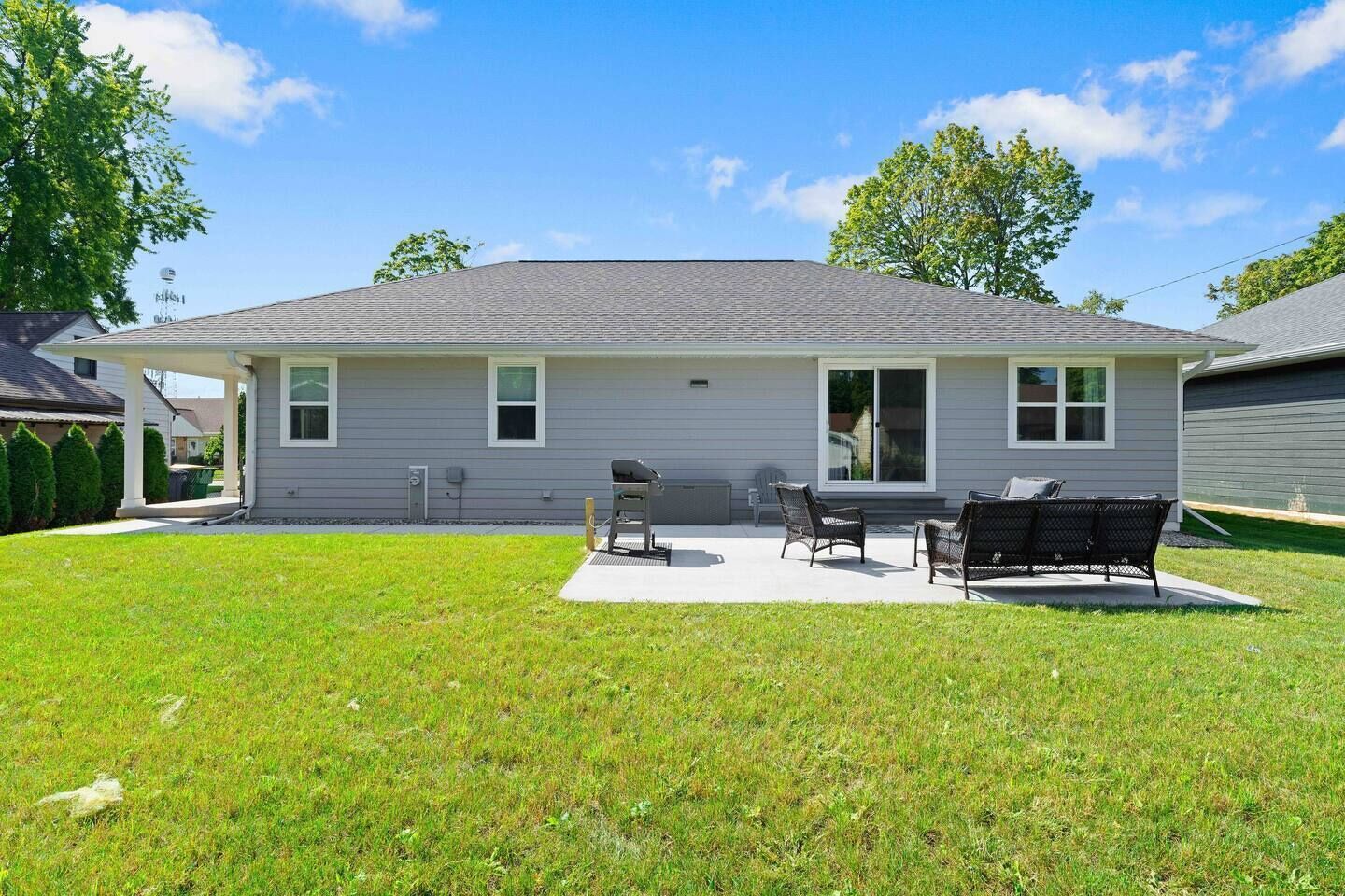 A single-story house with a covered patio area featuring a grill, two chairs, and a table.