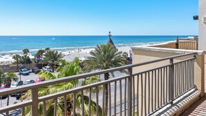 A balcony with a view of a beach, palm trees, and a lighthouse.