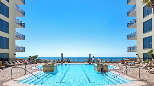 A swimming pool with a view of the ocean, surrounded by lounge chairs and a high-rise building.