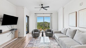 A modern living room with a flat-screen TV, two armchairs, a sofa, a coffee table, and a ceiling fan.