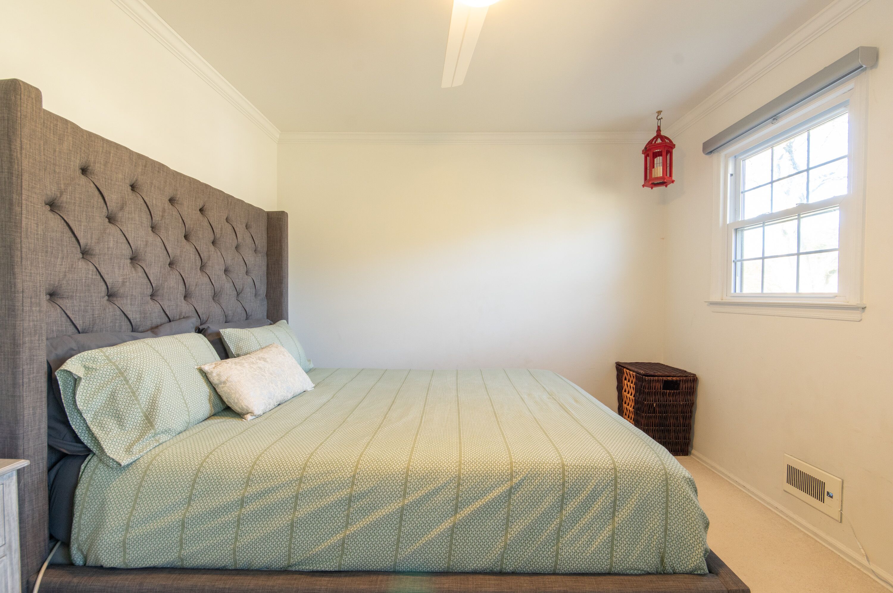 Un dormitorio con cabecera capitonada, cama con ropa de cama verde, un farolillo rojo y una ventana con persianas.