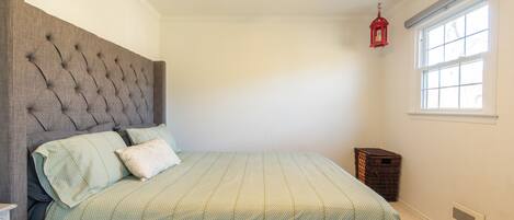 Un dormitorio con cabecera capitonada, cama con ropa de cama verde, un farolillo rojo y una ventana con persianas.