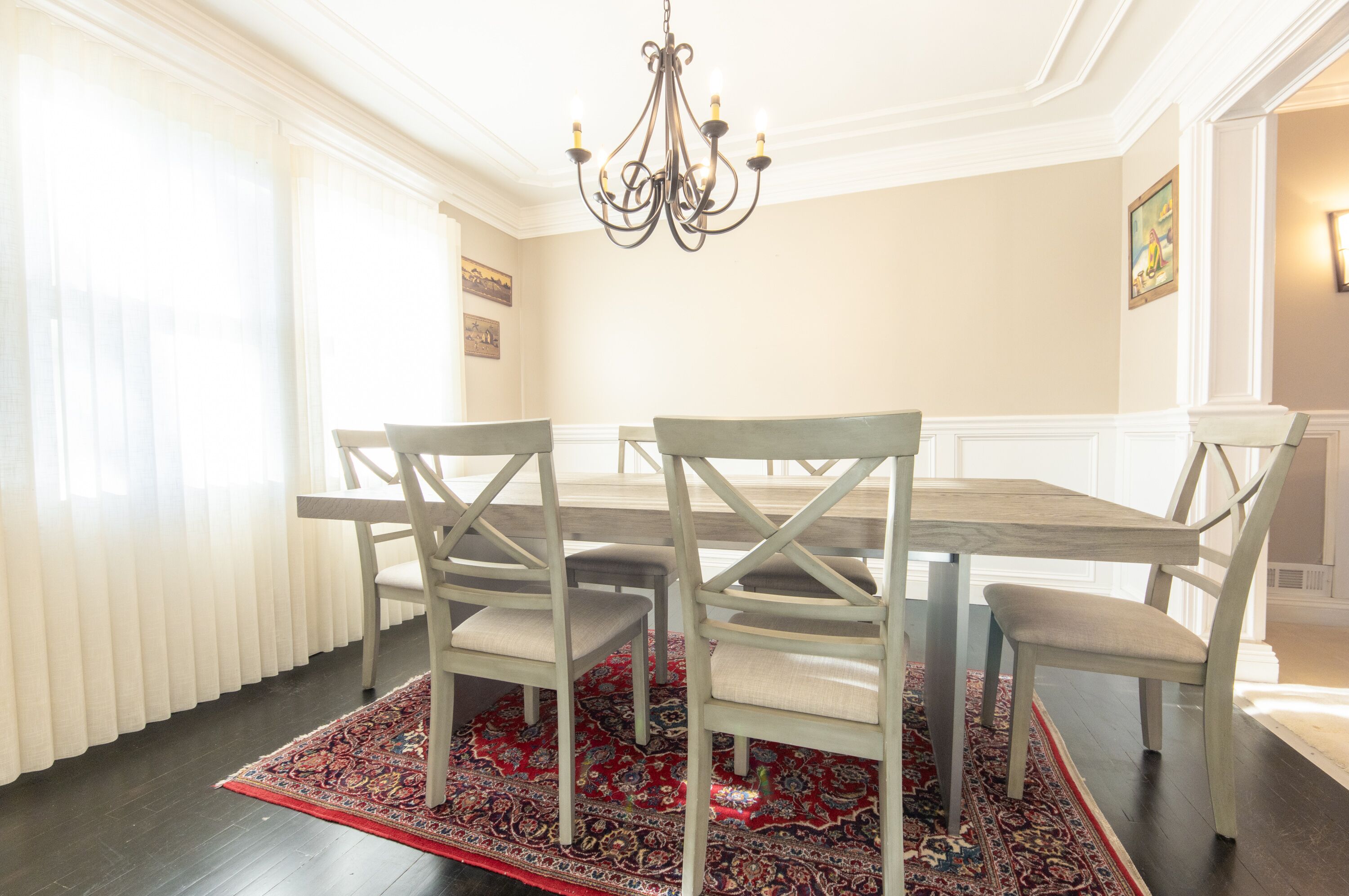 Un coin repas avec une table et des chaises en bois, un lustre et un tapis à motifs.