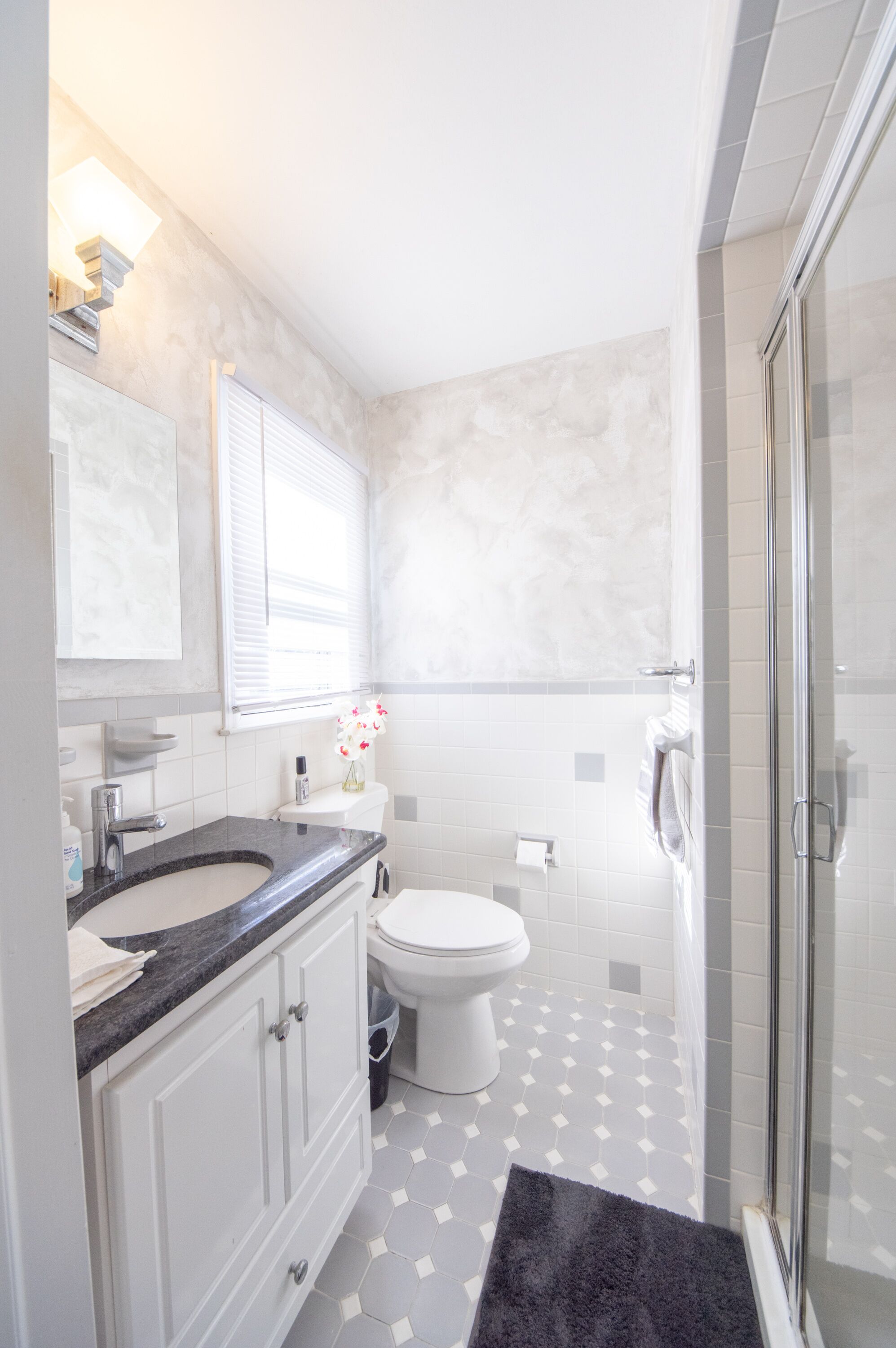 Une salle de bain avec des toilettes blanches, un lavabo doté d’un plan de travail en marbre et un espace douche.