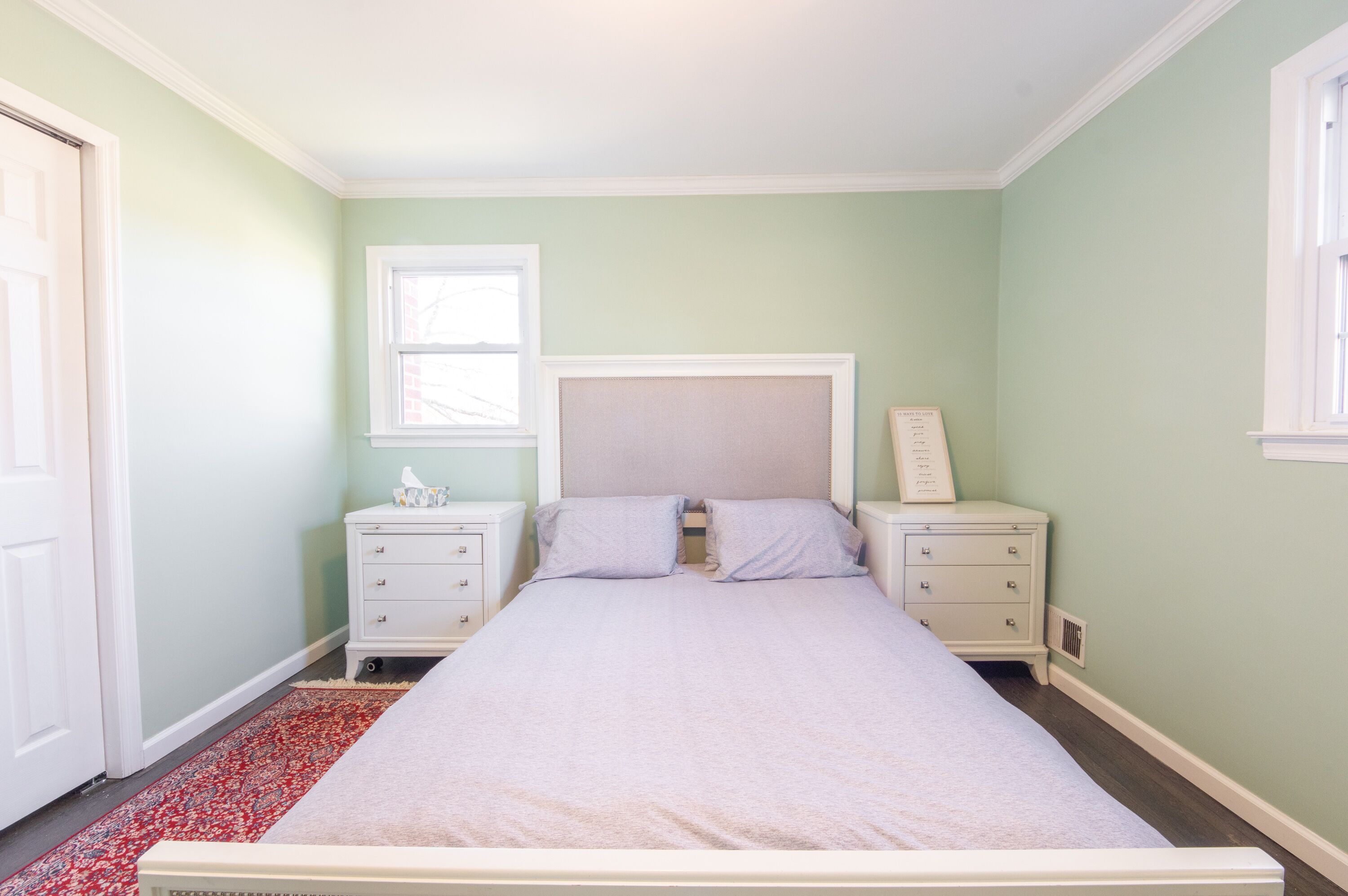 Un dormitorio con cama, dos mesitas de noche, una ventana y una puerta.