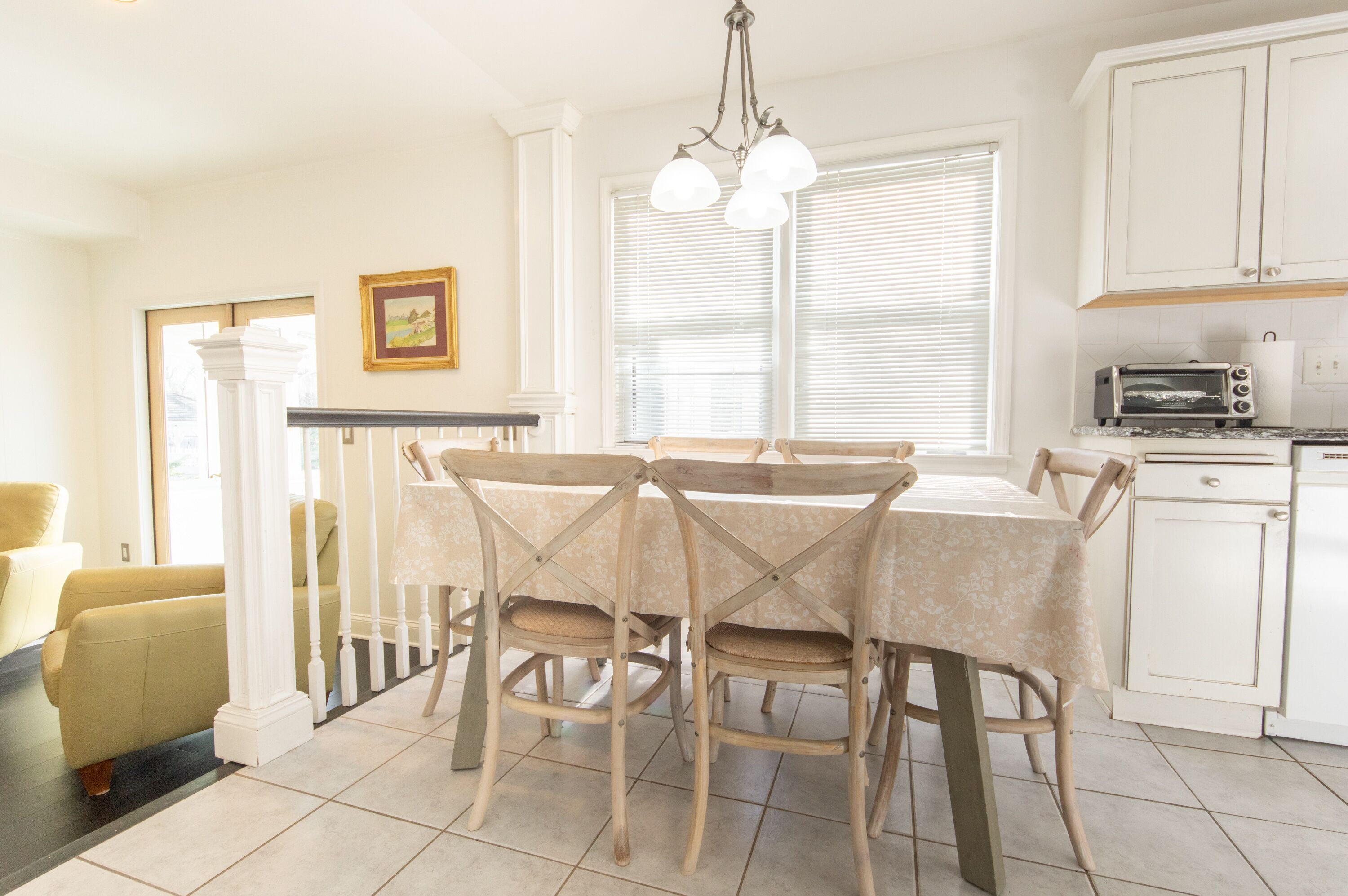 A dining area with a table set for four, a chandelier, and a kitchen with white cabinets and a toaster.