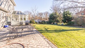 Eine Terrasse mit Glasveranda, Sitzgelegenheiten im Freien und einem Rasen.