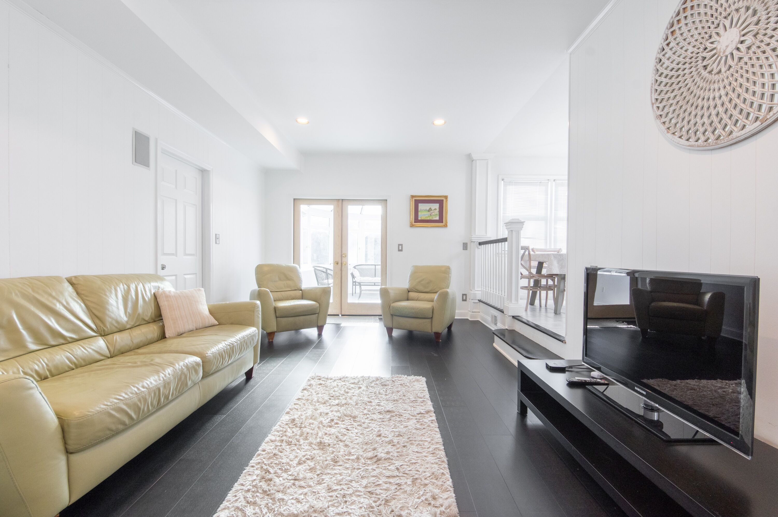 A living room with a beige leather sofa, two armchairs, a flat-screen TV, and a large decorative wall piece.