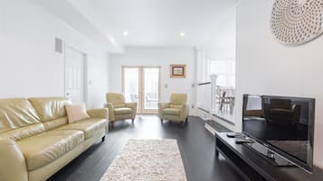 A living room with a beige leather sofa, two armchairs, a flat-screen TV, and a large decorative wall piece.