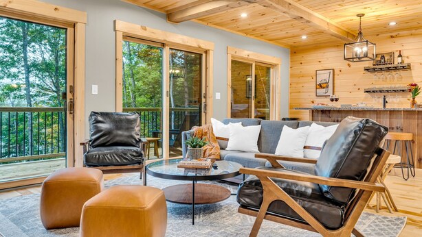 A spacious living area with a sofa, leather chairs, and a coffee table. Large windows and a balcony are visible.
