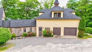 Une maison à deux étages avec une façade en pierre, un toit sombre et une allée gravillonnée.