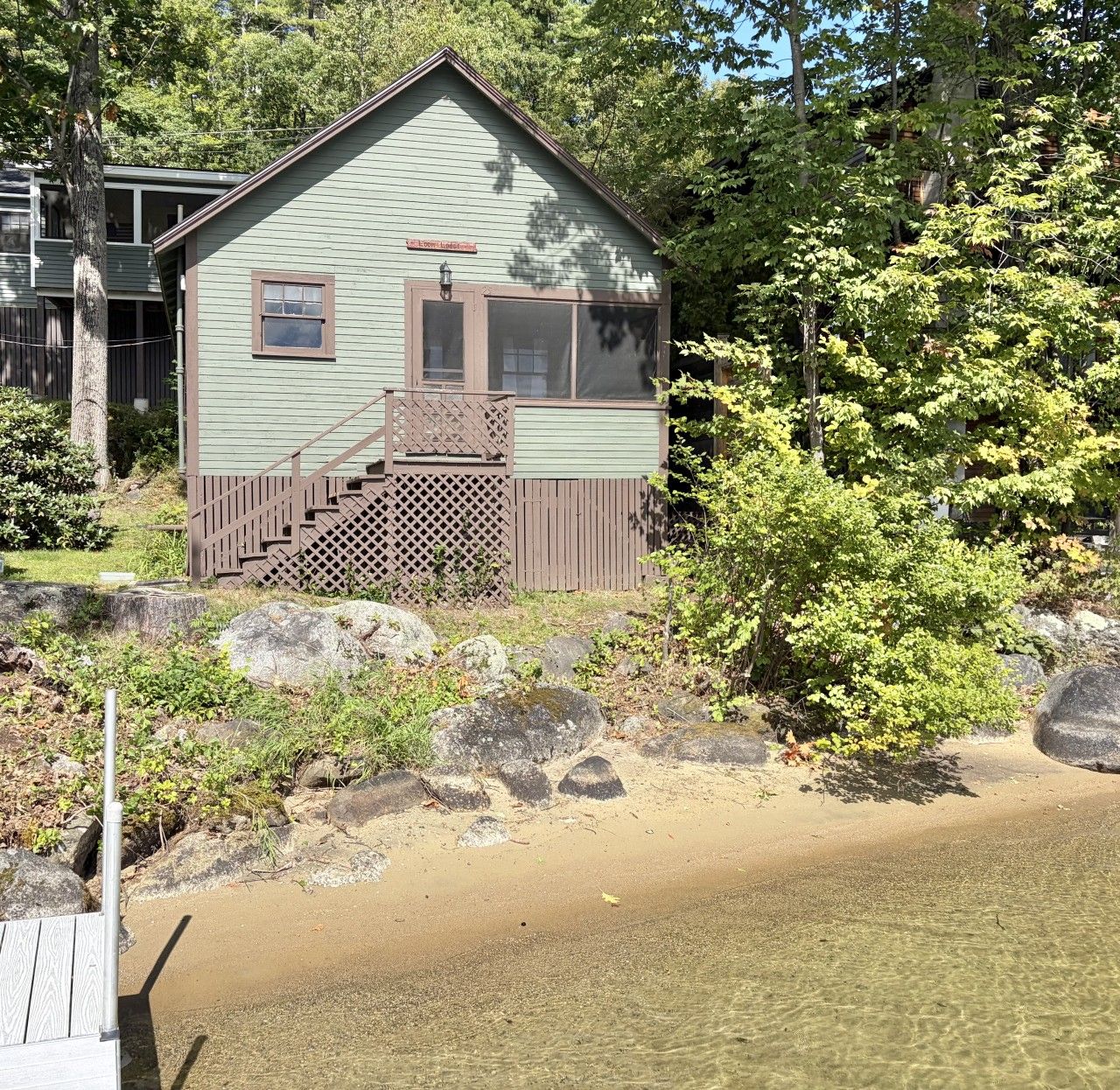 A cabin with a wooden deck, a staircase, and a view of a body of water.