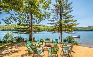 A lakeside seating area with green Adirondack chairs and a fire pit. - Loon Lodge - Waterfront Cabin (Holderness)
