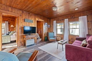 L’intérieur chaleureux d’un chalet, avec un revêtement mural en bois, un téléviseur, un canapé et un fauteuil.