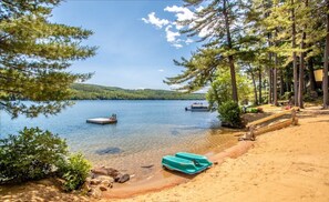 A beach with clear water, a dock, and boats. - Bear Cub Cabin- Waterfront Cabin (Holderness)