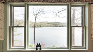 Una habitación con un ventanal grande con vista a un lago, un estampado de papel tapiz floral y unos binoculares en el alféizar.