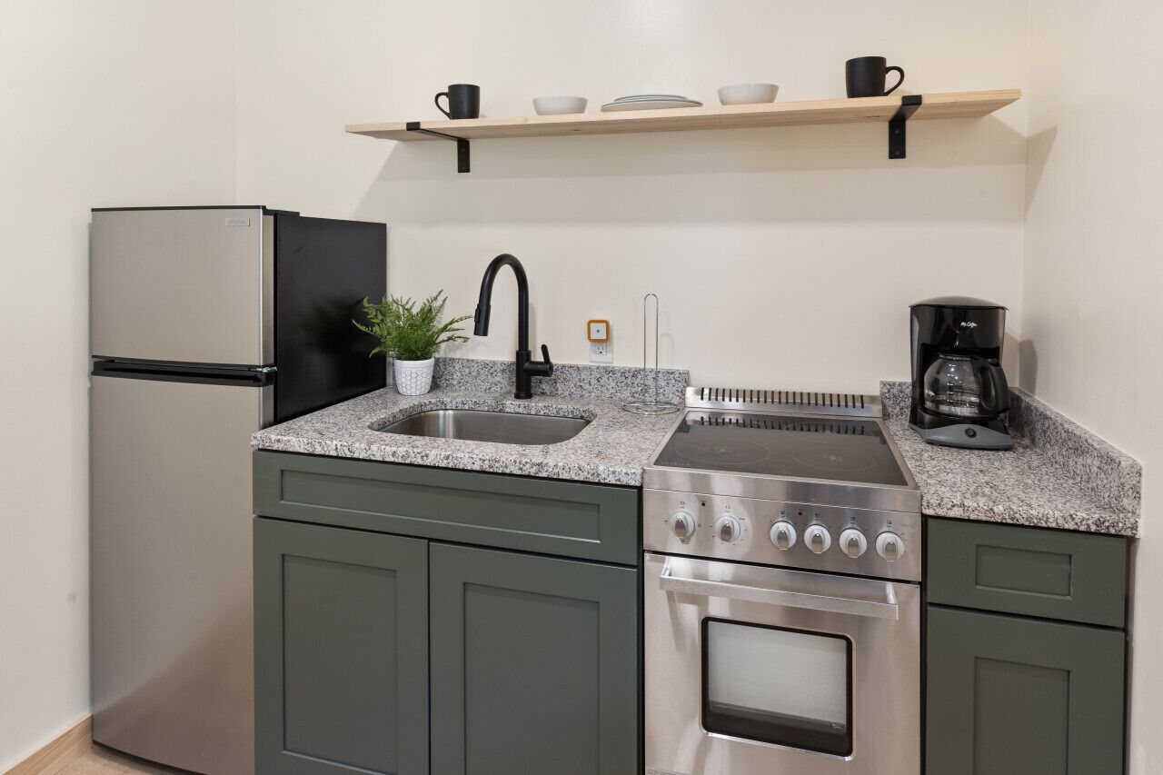 Cocina compacta con refrigerador de acero inoxidable, horno empotrado, lavamanos y cafetera.