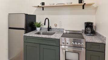 Cocina compacta con refrigerador de acero inoxidable, horno empotrado, lavamanos y cafetera.