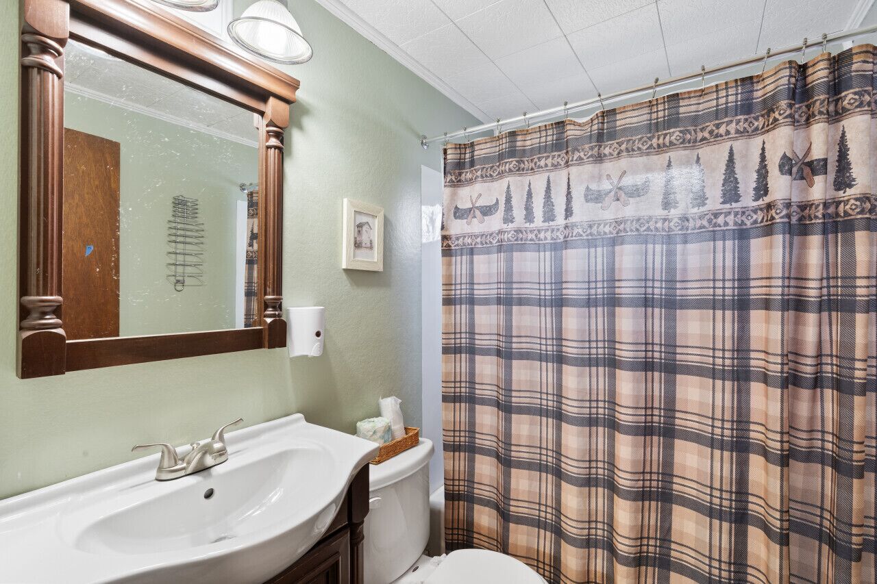 A bathroom with a white sink, a mirror, a toilet, and a plaid shower curtain.