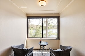 A corner room with a large window, wicker chairs, a small table, and a ceiling light. - Squam Lake 3 bed 3 bath (Suite #7) (Holderness)