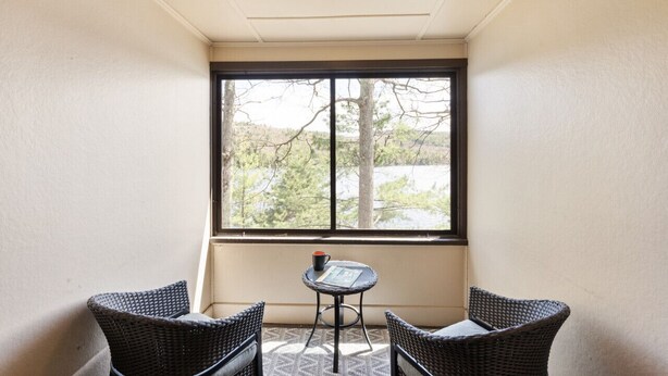 A room with a large window, wicker chairs, a small table, and a ceiling light. - Waterfront 3 bed/3 bath on Squam (#1) (Holderness)