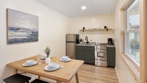A compact kitchen with a dining area, featuring a wooden table set for four, a refrigerator, a stove, and a coffee maker. - Waterfront 3 bed/3 bath on Squam (#1) (Holderness)