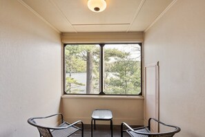 Habitación de esquina con ventana que da a un lago y árboles, dos sillones de mimbre y una mesita.