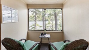 A room with a large window, wicker chairs, a small table with a vase and a newspaper, and a framed sign on the wall. - Waterfront 2 bed 2 bath rental (Suite 2) (Holderness)