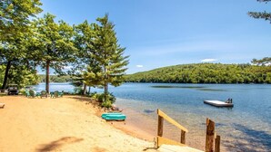 A beach with a wooden dock, a row of chairs, and a small boat. - Waterfront 2 bed 2 bath rental (Suite 2) (Holderness)