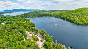 Uma propriedade à beira do lago com uma estrada que leva a um edifício, cercada por vegetação densa e uma grande extensão de água.