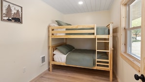 Quarto com beliche, janela, um quadro na parede e uma tomada.