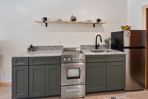 Eine Küche mit einem Edelstahlbackofen, einer Spüle und einem Kühlschrank. Über der Arbeitsplatte befinden sich Holzregale mit einer kleinen Baumdekoration und einer Tasse.