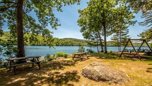 A lakeside camping area with picnic tables, a swing set, and a large rock. - Squam waterfront 2 bed 2bath (Suite 9) (Holderness)