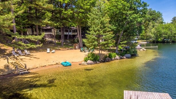 A lakeside property with a sandy beach, a wooden dock, and a building with a balcony overlooking the water. - Squam waterfront 2 bed 2bath (Suite 9) (Holderness)