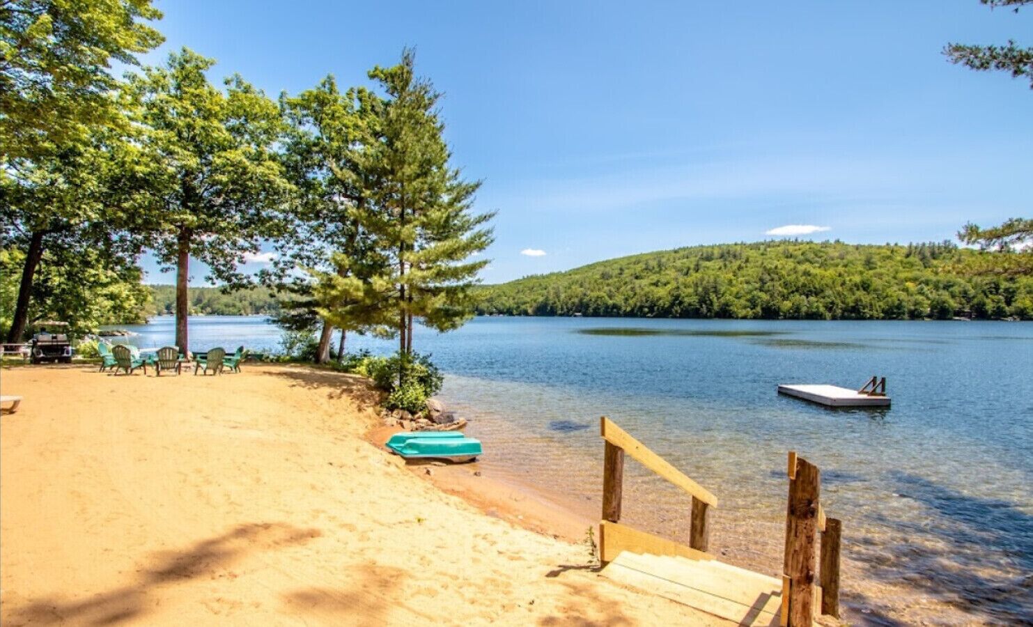 A beach with a sandy area, a row of green chairs, a small boat, and a wooden dock.
