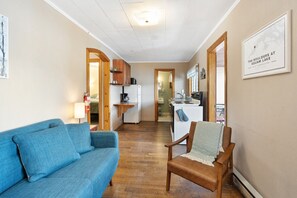 Ein gemütlicher Wohnbereich mit einem blauen Sofa, einem Holzstuhl, einer Küchenzeile und einer gerahmten Karte an der Wand.