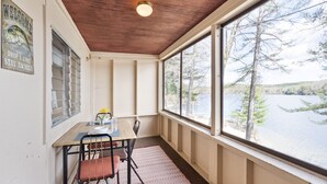 Ein Zimmer mit Holzboden, einem Tisch mit Stühlen, einem Fenster mit Blick auf Bäume und Wasser sowie einem Poster an der Wand.