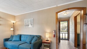 Ein Wohnzimmer mit blauem Sofa, einer Lampe, einem Bücherregal und einem Bild an der Wand.