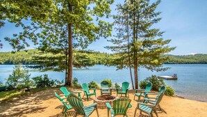 Un área de descanso junto al lago con sillones Adirondack verdes y un brasero, rodeada de árboles y vistas al lago.