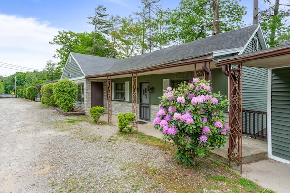 A rustic cabin with a porch, surrounded by gravel and greenery.