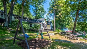 A wooden swing set in a backyard with a house in the background. - 2 Bedroom Rental on Squam Lake (Suite 4) (Holderness)