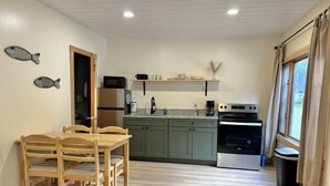 Una cuina compacta amb armaris de fusta, una taula de dinar amb caires i una finestra amb cortines.