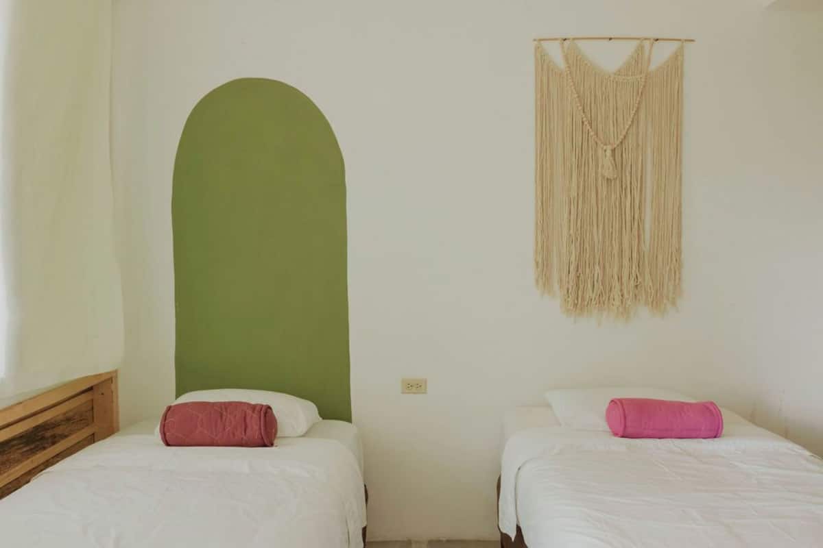 Een kamer met twee bedden, een groene boogdoorgang en een macramé wanddecoratie.